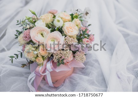 A large flower arrangement in a pink hat box was created by a florist for a wedding gift. White Freesia , pink Ranunculus asiaticus, eustoma flowers, roses and eucalyptus in a bouquet.