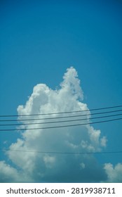A large, fluffy cumulus cloud dominates the sky, partially obscured by a series of dark overhead power lines stretching across the frame