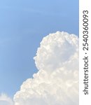 Large, fluffy white cloud against a bright blue sky, illuminated by sunlight, creating soft shadows and enhancing its texture. The sky is mostly clear, adding a calm and serene atmosphere to the scene