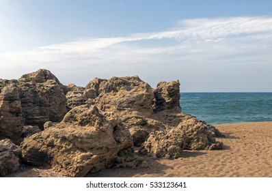 Large formation of rocks on shoreline between beach and ocean against blue sky and white clouds - Powered by Shutterstock