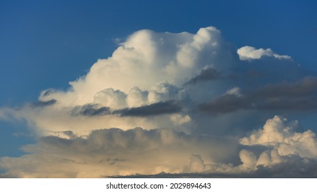 Large forming cumulonimbus rain cloud contrasted against a vibrant blue sky rising up and lit up from below at sunset 