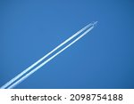Large four engine passenger supersonic aircraft flying from left to right high in clear blue cloudless sky leaving bright long white trail