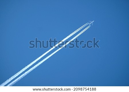 Large four engine passenger supersonic aircraft flying from left to right high in clear blue cloudless sky leaving bright long white trail