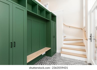 A large foyer with a vibrant green storage unit, white oak bench and stairs, and a black and white pattern tile flooring.