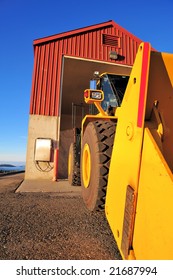 Large front loading tractor and salt storage building against a clear blue sky.