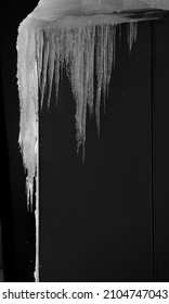 Large Frozen Icicle Back Lit By Sun And Dripping Or Melting Off Of Dark Rectangular Roof And Wall Showing Signs Of Spring On A Warm Winters Day With Sun Shining Vertical Format Framed Room For Type 