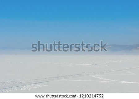 a large frozen lake covered with snow, a wheel track on a snowy field; thick fog over a distant rocky shore, a clear frosty morning; arctic landscape; Siberia; Baikal in winter; Russia