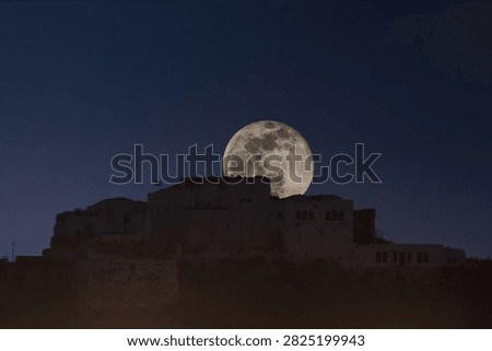 A large full moon rises behind an ancient stone fortress or castle silhouetted against a deep blue night sky.