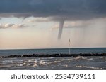 A large funnel cloud is seen over the ocean. The sky is cloudy and the water is choppy