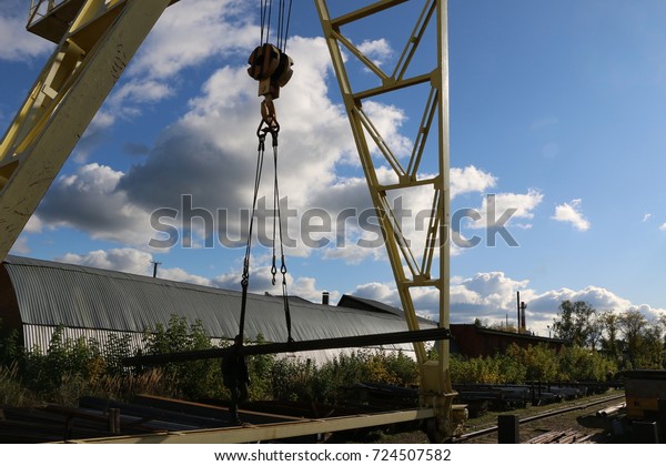 A large gantry crane made of metal colored yellow\
in the background of a bright blue sky with clouds close-ups moves\
the cargo