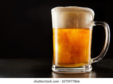 Large Glass Mug Of Effervescent Chilled Glitter Draft Beer With A Good Frothy Head Over A Reflective Black Background With Copy Space