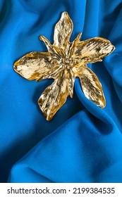 Large Gold Flower Shaped Brooch On Blue Draped Fabric Closeup