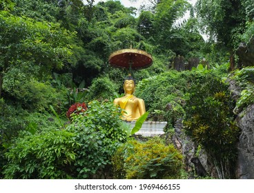 A Large Golden Buddha Sitting Meditating With An Umbrella In The Middle Of The Jungle Surrounded By Nature.