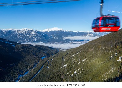 A large gondola car streaking by with the valley in between Whistler and Blackcomb in the background.