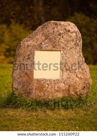 Large granite stone with empty metal plate lying on a green grass