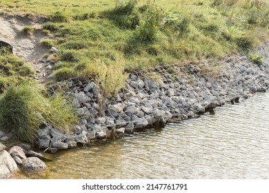 Large granite stones on the river bank. The edge of the river bank, reinforced with large stones against erosion. View of stone paving on the embankment, strengthening the river bank