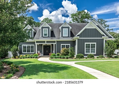 A large gray craftsman new construction house with a landscaped yard and leading pathway sidewalk on a sunny day with blue skies and clouds. - Shutterstock ID 2185631379