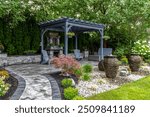 Large gray pergola on pavers with stone fireplace and waterfall urns for backyard oasis landscape design