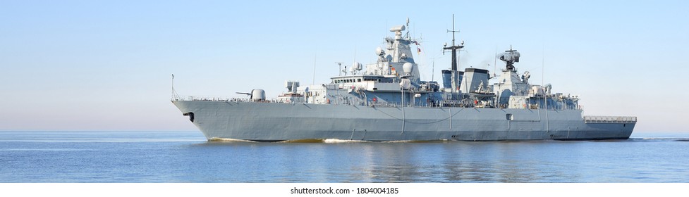 Large grey modern warship sailing in still water. Clear blue sky. Baltic sea, Germany. Global communications, international security, industry, transportation theme. Panoramic view