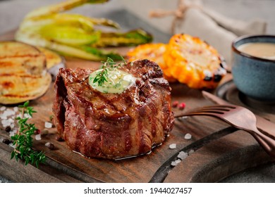 Large grilled Filet Mignon steak with butter and thyme served on a wooden board. Grilled meat dish with vegetables