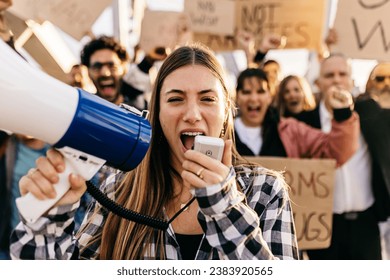 Large group of diverse people manifesting against war or attack on a country. Female activist using megaphone outdoors. Stop war signs and banners in a peace demonstration
