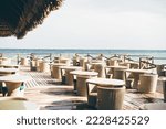 A large group of empty wicker tables and chairs in an outdoor tropical bar; a street cafe next to the ocean, in a luxury resort, no people, canopy bungalow