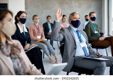 Large Group Of Entrepreneurs Attending Business Seminar And Wearing Protective Face Masks Due To COVID-19 Pandemic. Focus Is On Businessman With Raised Hand. 