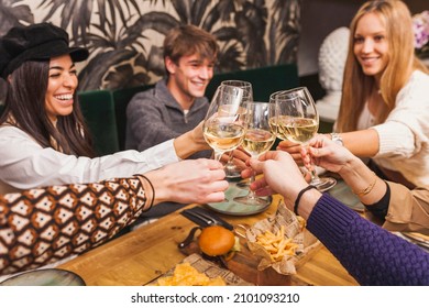 Large Group Of Friends Raising Their Glasses For A Toast At A Dinner Party. Beautiful Caucasian Stylish Millennial Young People Drinking And Enjoying At Restaurant.