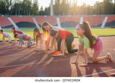 A large group of  girls, are taught by a coach at the start before running at the stadium during sunset. A healthy lifestyle. - Powered by Shutterstock