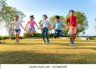 Large group of happy Asian smiling kindergarten kids friends holding hands playing and jumping together during a sunny day in casual clothes at city park. Multi-ethnic children group, outdoor. - Shutterstock ID 1673662930