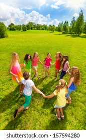 Large group of happy girls play roundelay and stand in circle in the park on the green grass on sunny summer day top view