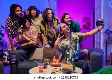 Large group of happy young intercultural friends gathered by couch and small served table taking selfie while enjoying home party - Powered by Shutterstock