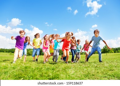 Large Group Of Kids, Friends Boys And Girls Running In The Park On Sunny Summer Day In Casual Clothes