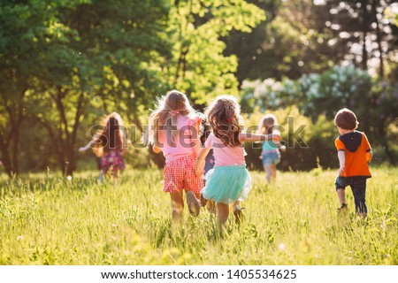 Large group of kids, friends boys and girls running in the park on sunny summer day in casual clothes 