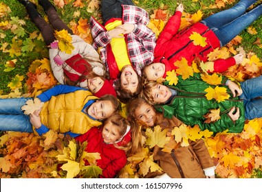 Large Group Of Kids Laying In The Grass With Maple Leaves All Over Them On Autumn Day