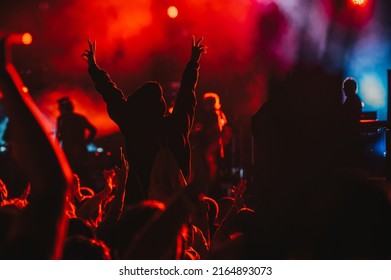 Large Group Of People In A Concert Crowd Enjoying Live Performance On A Music Festival At Night. Audience Raising Hands Up.