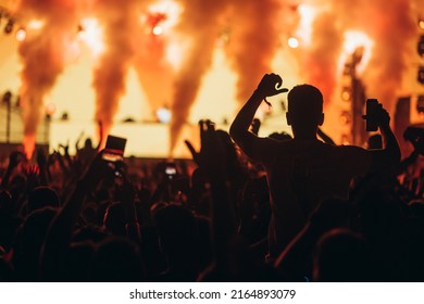 Large Group Of People In A Concert Crowd Enjoying Live Performance On A Music Festival At Night. Audience Raising Hands Up.