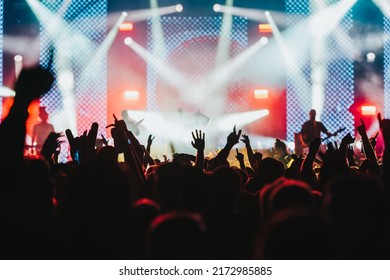 Large Group Of People In A Concert Crowd Enjoying Live Performance On A Music Festival At Night. Audience Raising Hands Up.