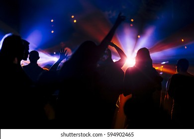 Large group of people on a dance floor. There is a very vivd colorful backlight. 
