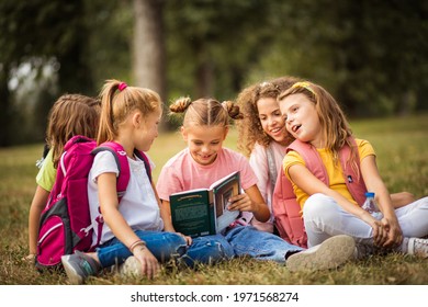  Large group of school kids having fun in nature. Little girl reading book to her friends.