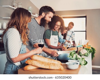 Large Group Of Six Friends Preparing Food For A Cooking Class At Table At Home Or In A Small Culinary School