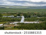 A large group of tourists gathered around a geyser in Haukadalur, Iceland, witnessing a spectacular eruption surrounded by vast green plains and distant mountains.