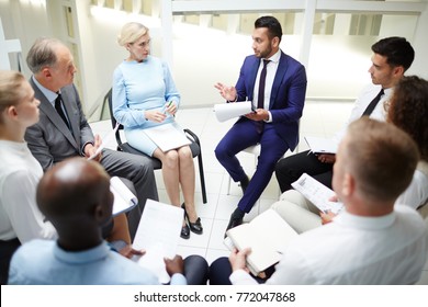 Large Group Of Young And Mature Colleagues In Formalwear Sitting In Circle At Session Or Seminar And Discussing Reports