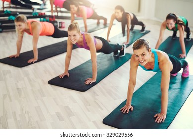 Large Group Of Young Women Working Out In A Gym Doing Push Ups In An Aerobics Class In A Health And Fitness Concept