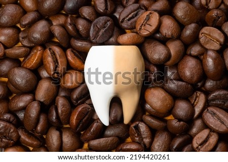 Large half-white and half-brown tooth on a pile of roasted coffee beans. Coffee staining and teeth whitening concept.