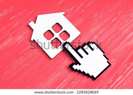 Large hand-shaped mouse cursor figurine clicks a flat house shape placed on a red wooden background, representing the idea of building appealing and intuitive graphical interfaces.