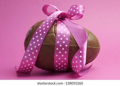 Large Happy Easter chocolate Easter egg with pink polka dot ribbon tied in a bow against a pretty feminine pink background. - Powered by Shutterstock