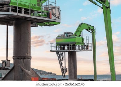 Large harbor cranes operating efficiently, handling cargo at a bustling commercial dock under a vibrant sunset sky