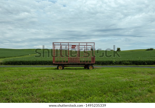 Large hay bale trailer sitting\
empty in vast field waiting to be used for harvest on an overcast\
day