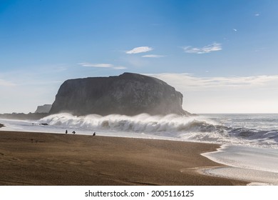 Large haystack rock with crashing waves and birds on the beach in California